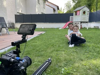 Deux garçons jouent dans le jardin d'une maison. En premier plan, une caméra.